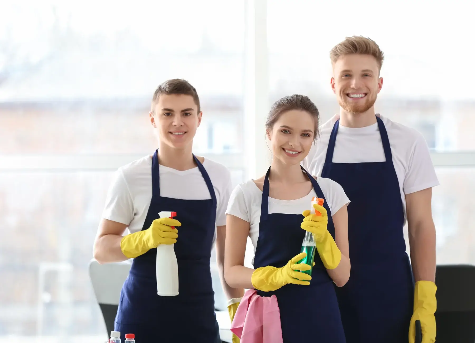 Three Pro Clean Melbourne cleaners in aprons holding spray bottles and cloths